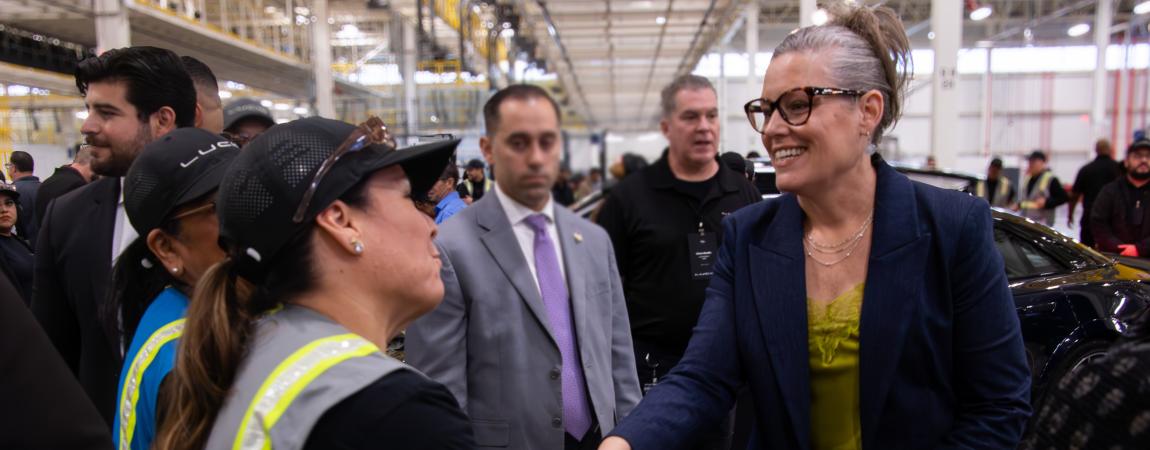 Governor Katie Hobbs meeting with a Lucid employee wearing a high visibility vest surrounded by people conversating in the car factory.