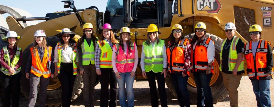 Governor Hobbs and others wearing P.P.E. in front of a large bulldozer.