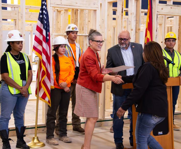 Governor Katie Hobbs shaking a womans hand after speaking at a podium surrounded by construction workers.