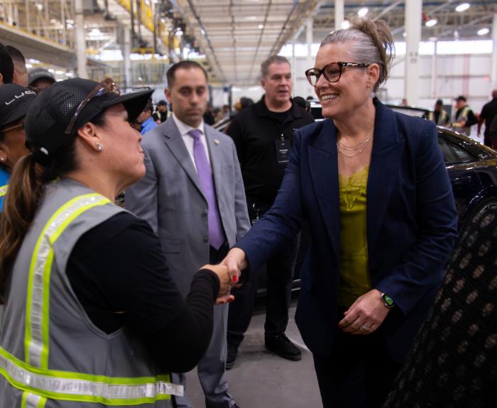 Governor Katie Hobbs meeting with a Lucid employee wearing a high visibility vest surrounded by people conversating in the car factory.