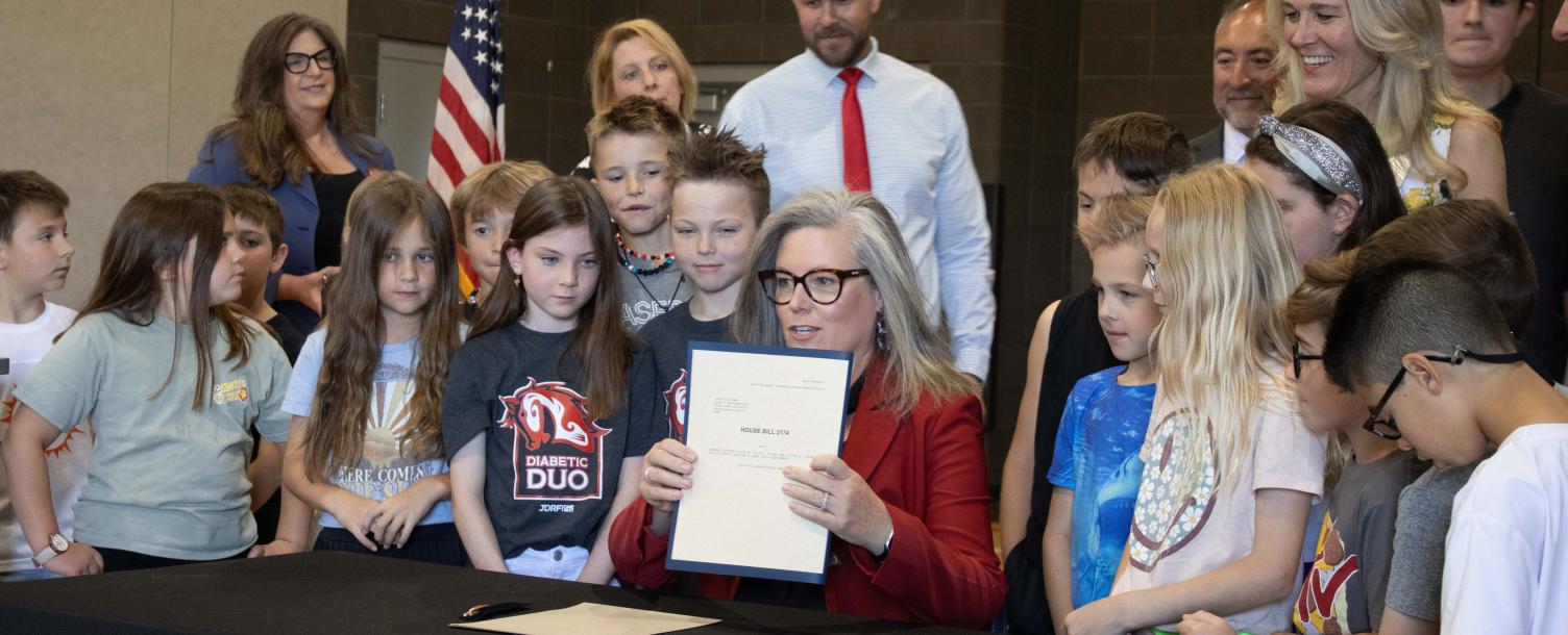 Governor Katie Hobbs presenting a bill surrounded by children.