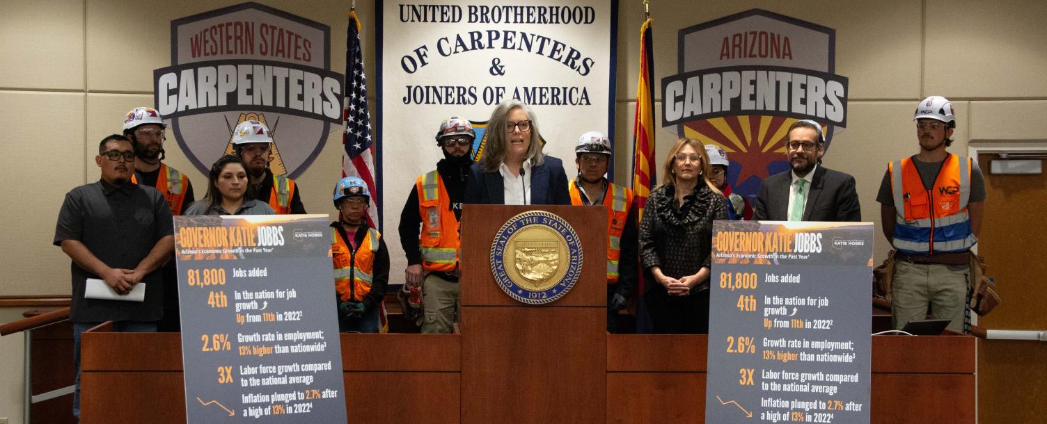 Governor Katie Hobbs speaking on a podium surrounded by carpenters.